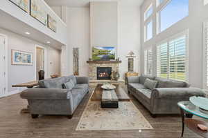 Living area featuring a towering ceiling, a stone fireplace, and wood finished floors
