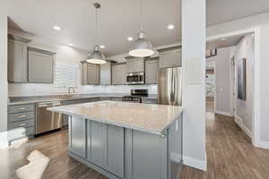 Kitchen featuring gray cabinetry, light stone counters, light wood-style flooring, appliances with stainless steel finishes, and decorative light fixtures