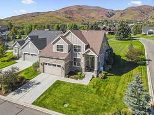 View of front of home with board and batten siding, stone siding, a shingled roof, concrete driveway, and a front lawn
