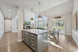 Kitchen featuring light stone counters, pendant lighting, a stone fireplace, open floor plan, and dark wood-style flooring