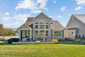 Rear view of house with board and batten siding, a shingled roof, a lawn, and a patio area