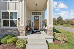 Property entrance with board and batten siding, a porch, stone siding, a mountain view, and a lawn