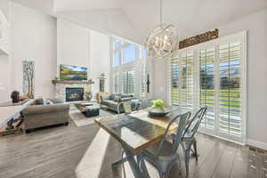 Dining room featuring a stone fireplace, wood finished floors, high vaulted ceiling, and a chandelier