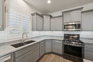 Kitchen featuring gray cabinetry, appliances with stainless steel finishes, light stone counters, light wood-style flooring, and decorative backsplash