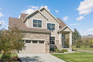 Craftsman house with board and batten siding, a shingled roof, driveway, and stone siding