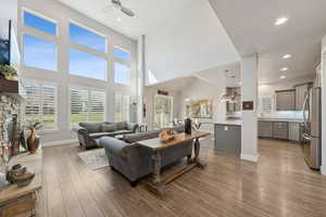 Living area featuring ceiling fan, a stone fireplace, dark wood-style floors, recessed lighting, and a high ceiling