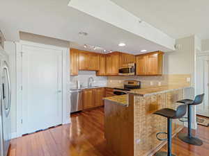 Kitchen with backsplash, stainless steel appliances, a kitchen bar, dark wood-style flooring, and brown cabinets