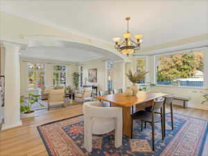 Dining space featuring ornate columns, arched walkways, crown molding, light wood-style floors, and a chandelier