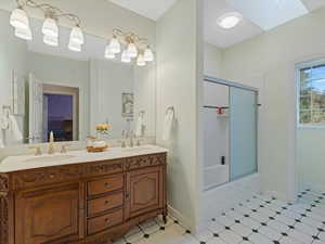 Ensuite bathroom featuring double vanity, bath / shower combo with glass door, and a skylight