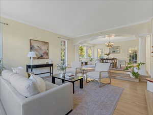 Living area with ornamental molding, a chandelier, light wood-style floors, healthy amount of natural light, and ornate columns