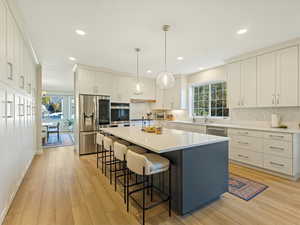Kitchen with appliances with stainless steel finishes, a kitchen island with sink, hanging light fixtures, a kitchen bar, and white cabinets