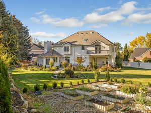 Rear view of property featuring a garden, a balcony, stucco siding, and a chimney