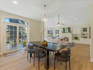 Dining space with a glass covered fireplace, light wood-style flooring, vaulted ceiling, recessed lighting, and ceiling fan