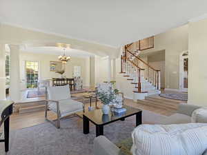 Living area with ornamental molding, a chandelier, wood finished floors, stairs, and arched walkways