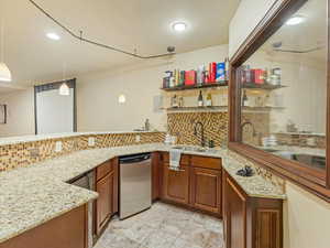 Kitchen with hanging light fixtures, brown cabinets, light stone countertops, open shelves, and decorative backsplash