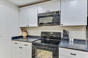 Kitchen with dark countertops, black appliances, and white cabinets