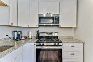 Kitchen with stainless steel appliances, white cabinetry, and light stone countertops
