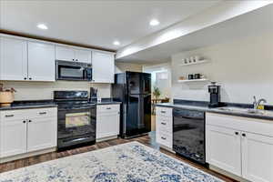 Kitchen featuring black appliances, white cabinetry, open shelves, recessed lighting, and dark countertops