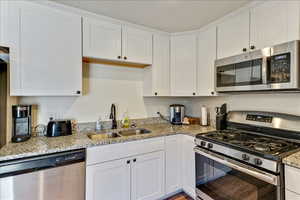 Kitchen featuring stainless steel appliances, white cabinetry, and light stone countertops