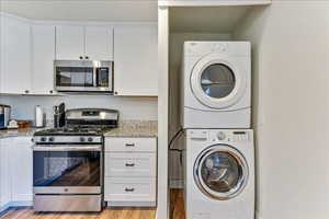 Kitchen with appliances with stainless steel finishes, white cabinetry, stacked washing machine and dryer, and light stone countertops