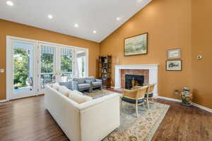 Living room with recessed lighting, high vaulted ceiling, dark wood finished floors, a tile fireplace, and french doors