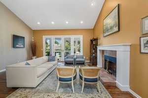 Living room with lofted ceiling, a tile fireplace, recessed lighting, wood finished floors, and french doors