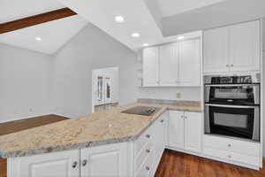 Kitchen with dark wood-style flooring, double oven, white cabinetry, vaulted ceiling, and recessed lighting