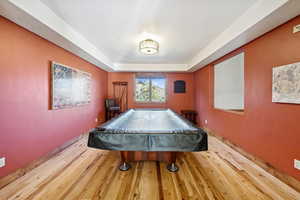 Game room with wood-type flooring, a tray ceiling, and pool table