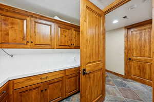Kitchen with tile countertops, brown cabinetry, stone tile flooring, and recessed lighting