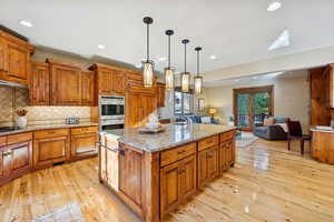 Kitchen featuring brown cabinets, decorative backsplash, hanging light fixtures, open floor plan, and recessed lighting