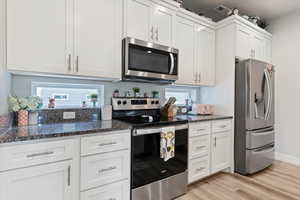 Kitchen with can lighting, white cabinetry, stainless steel appliances, an island with sink, and granite countertops