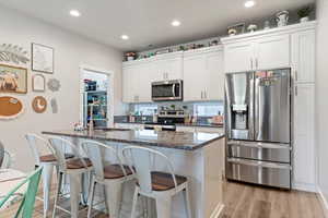 Kitchen with can lighting, white cabinetry, stainless steel appliances, an island with sink, and granite countertops