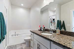 Bathroom featuring a vanity, granite countertops, tub, shower and toilet