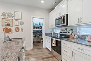 Kitchen with can lighting, white cabinetry, stainless steel appliances, an island with sink, and granite countertops