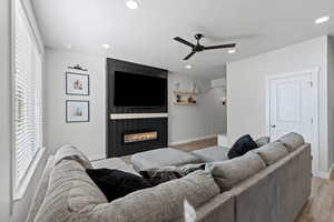 Living room featuring light wood-type flooring, a fireplace, recessed lighting, a ceiling fan, and a textured ceiling
