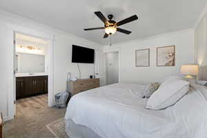 Bedroom with ornamental molding, light colored carpet, ceiling fan, and ensuite bath