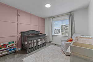 Bedroom with light colored carpet, a nursery area, and a decorative wall