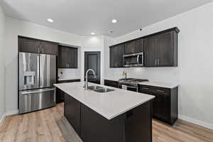 Kitchen featuring appliances with stainless steel finishes, tasteful backsplash, a kitchen island with sink, dark brown cabinets, and a textured ceiling