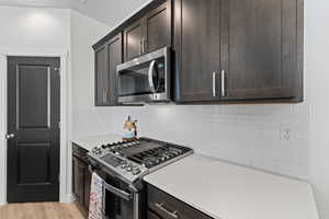 Kitchen with stainless steel appliances, dark brown cabinets, backsplash, and light wood-style floors