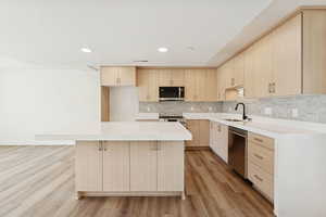 Kitchen featuring light brown cabinetry, light wood-style flooring, light stone counters, recessed lighting, and a kitchen island