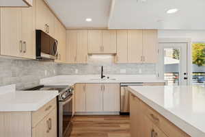 Kitchen with light brown cabinetry, stainless steel appliances, light wood-type flooring, recessed lighting, and tasteful backsplash