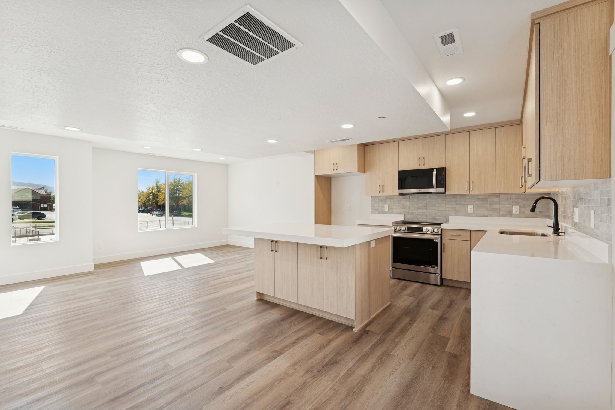 Kitchen featuring light brown cabinetry, a kitchen island, stainless steel appliances, decorative backsplash, and light wood finished floors