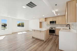 Kitchen featuring light brown cabinetry, a kitchen island, stainless steel appliances, decorative backsplash, and light wood finished floors