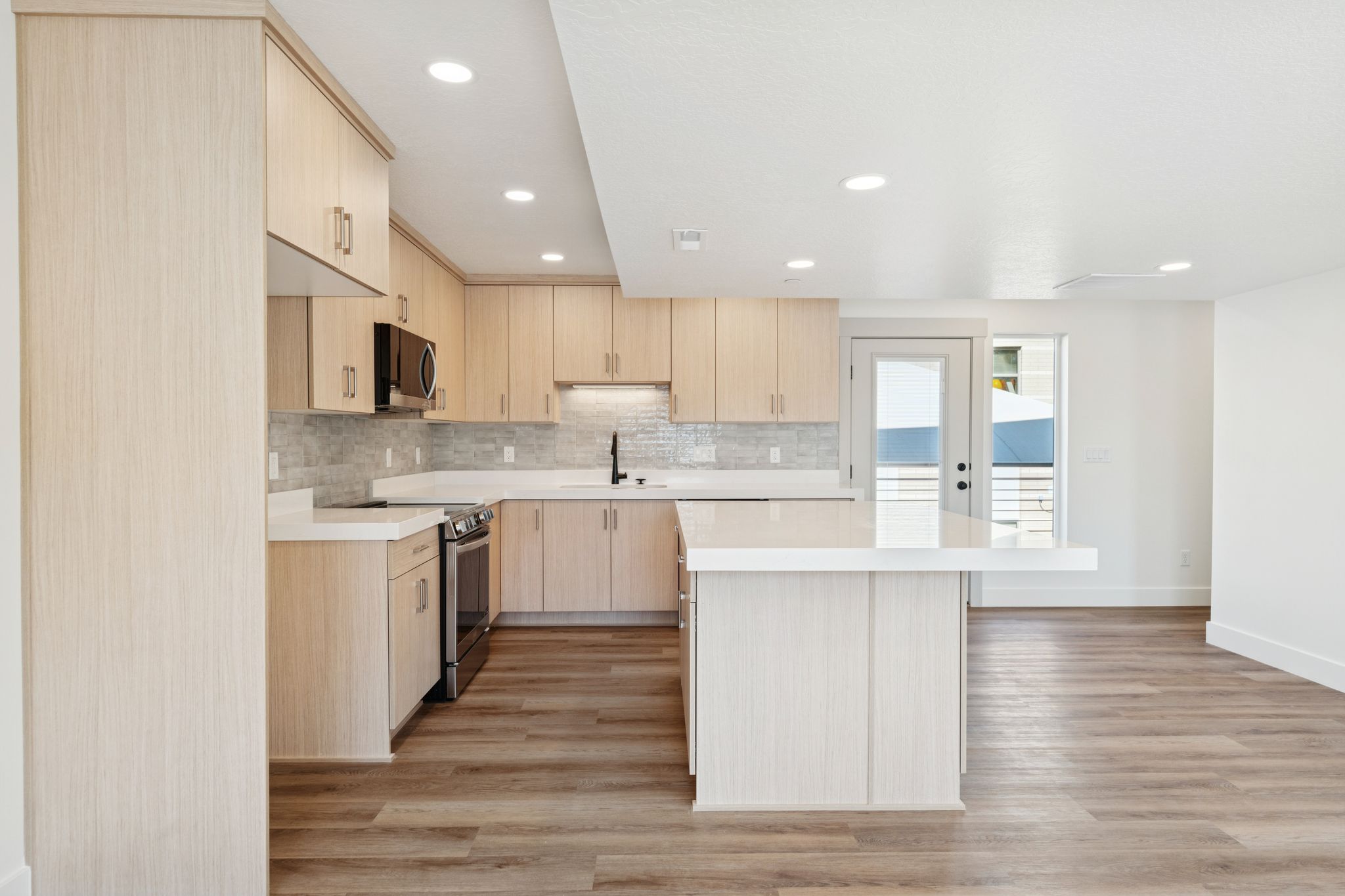 Kitchen with light brown cabinets, decorative backsplash, recessed lighting, modern cabinets, and appliances with stainless steel finishes