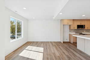 Kitchen featuring light countertops, tasteful backsplash, recessed lighting, light wood-style floors, and stainless steel microwave