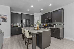 Kitchen featuring tasteful backsplash, a breakfast bar area, light stone counters, stainless steel appliances, and recessed lighting