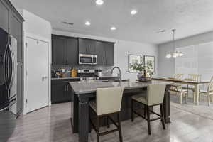 Kitchen featuring light stone countertops, a textured ceiling, hanging light fixtures, a kitchen island with sink, and tasteful backsplash