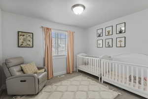 Bedroom featuring light carpet, a crib, and a textured ceiling