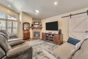 Living room with vaulted ceiling, a barn door, wood finished floors, a gasfireplace, and recessed lighting