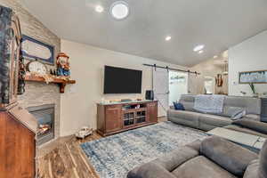 Living room with vaulted ceiling, a barn door, wood finished floors, a gas fireplace, and recessed lighting